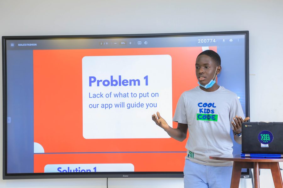 A young learner presenting his app idea on a large screen at a Cool Kids Code session