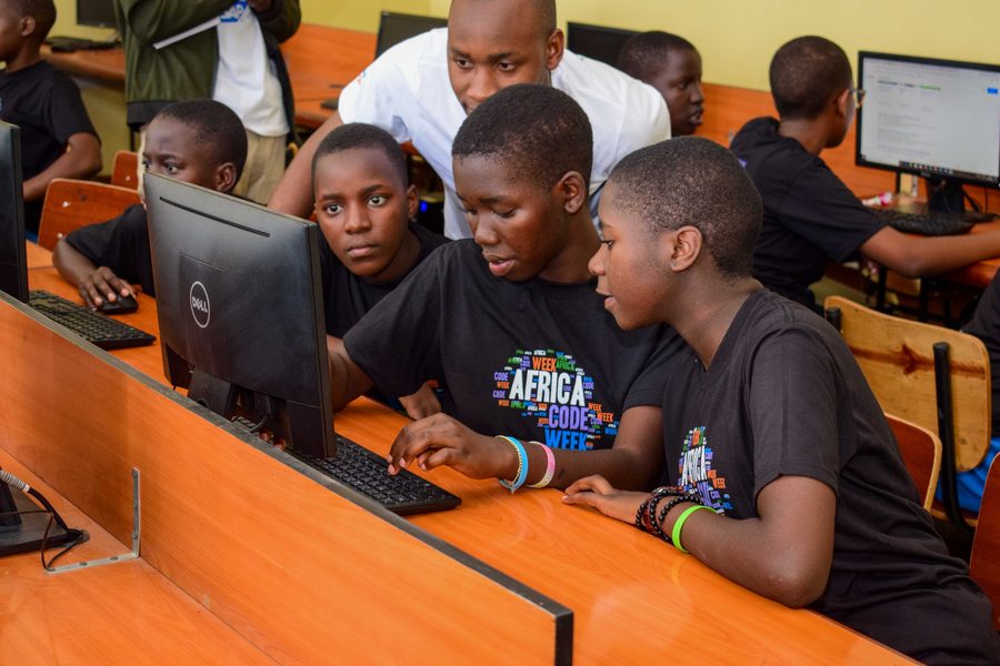Learners working together at computers during a coding session, with a teacher helping